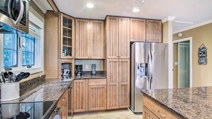 A kitchen with wooden cabinets, a stainless steel refrigerator, granite countertops, and a window with a view of trees. - Readfield Retreat w/ Lake Maranacook Views! (Readfield)
