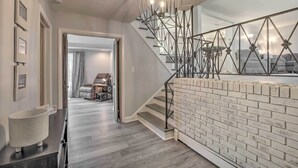 A modern interior with a staircase, a brick wall, and a dining area in the background. - Updated High Point Retreat w/ Pool & Backyard (High Point)