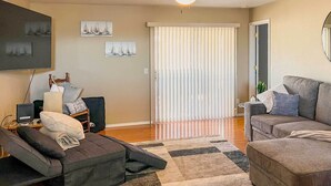 A living room with a sofa, a recliner, a coffee table, a TV, and a window with blinds.