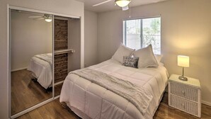 A bedroom with a bed, a nightstand, a ceiling fan, a window with blinds, and a mirror.