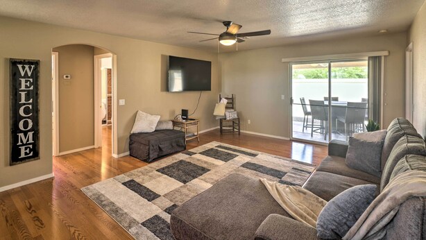 A living room with a sectional sofa, a flat-screen TV, a ceiling fan, and a large window with a view of the outdoors.