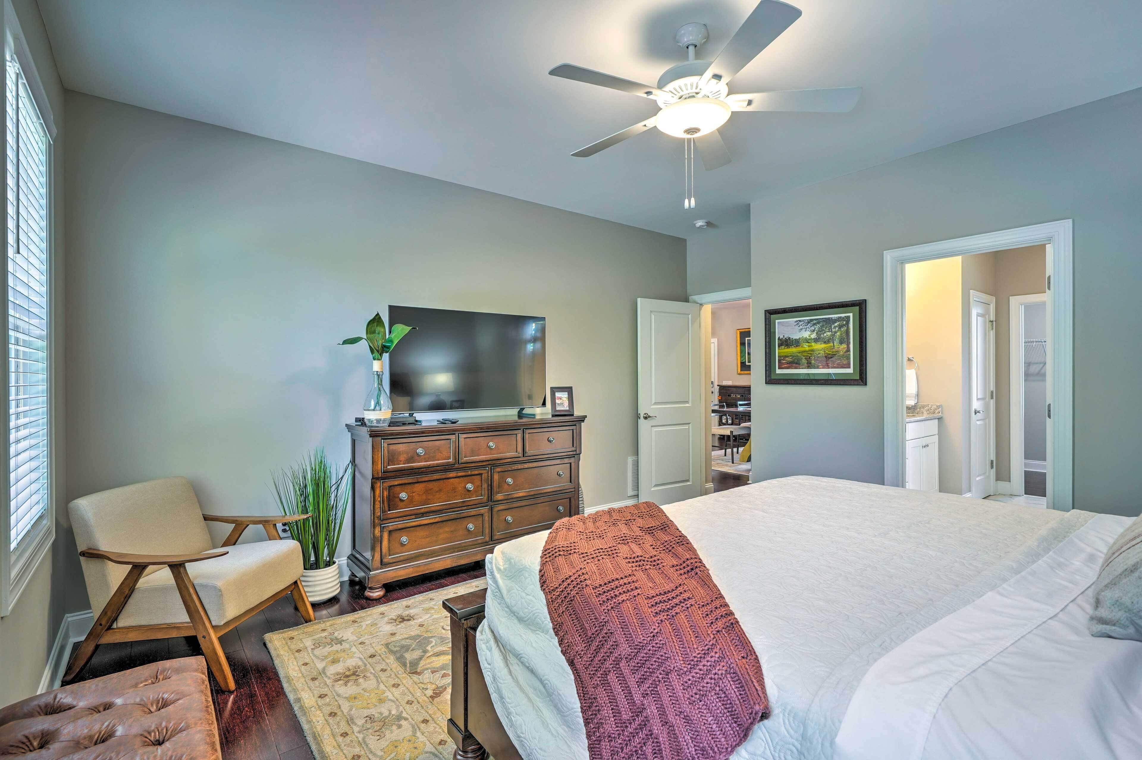A bedroom with a bed, a ceiling fan, a dresser, a TV, and a chair.