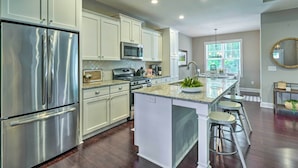 A modern kitchen with stainless steel appliances, white cabinetry, and a central island with stools. - Pinehurst Golf Paradise - 2 Mi to Clubhouse! (Pinehurst)