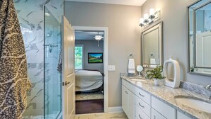 A bathroom with a glass shower, a bed in the background, a large mirror, and a sink with a marble countertop. - Pinehurst Golf Paradise - 2 Mi to Clubhouse! (Pinehurst)