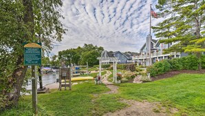 A waterfront property with a dock, a covered seating area, and a large house with a porch. - Breezy-chic Apartment - Steps to Geneva Lake! (Williams Bay)