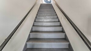 A staircase with a handrail, leading to a door with a large circular sign. - Breezy-chic Apartment - Steps to Geneva Lake! (Williams Bay)