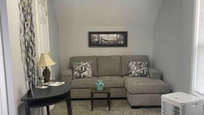 A living room with a sofa, a small table, a lamp, and a ceiling light. - Anoka 2 bedroom apt. in Historical Victorian House (Anoka)