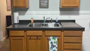 A kitchen with wooden cabinets, a black countertop, a sink, and a decorative towel. - Anoka 2 bedroom apt. in Historical Victorian House (Anoka)
