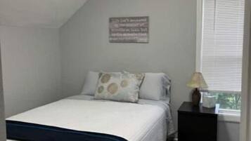 Une chambre à coucher avec un lit, une table de chevet, une fenêtre avec des stores et un luminaire au plafond.