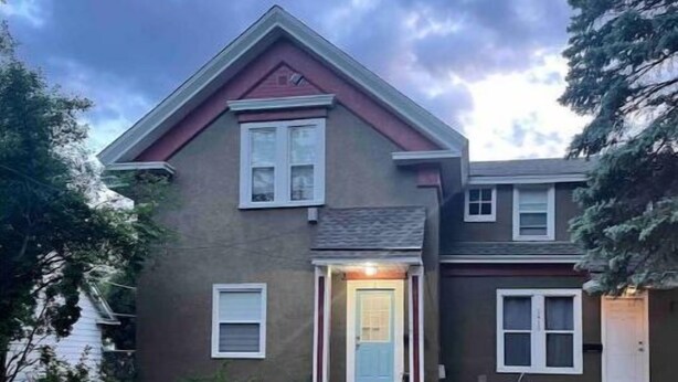 A two-story house with a front porch and a visible garage door. - Anoka 2 bedroom apt. in Historical Victorian House (Anoka)