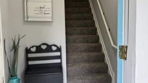 A hallway with a staircase, a framed certificate on the wall, a black bench with heart-shaped cutouts, and a potted plant. - Anoka 2 bedroom apt. in Historical Victorian House (Anoka)