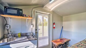 Cocina compacta con microondas, fregadero y estufa, un banco de madera y una ventana con persianas.
