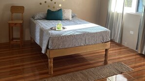 A bedroom with a wooden bed, a small wooden stool, a decorative wall, and a window with curtains.