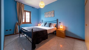 Una camera da letto con un letto, lampade sui comodini, una finestra con tende e un punto luce a parete.