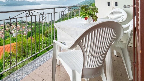 Un balcone con tavolo e sedie, affacciato su un lago e sulla vegetazione.
