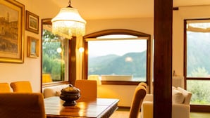A dining area with a table, chairs, and a chandelier. There are framed pictures on the wall and a view of mountains through a window. - Ca Furmiga by Wonderful Italy (Tremezzina)