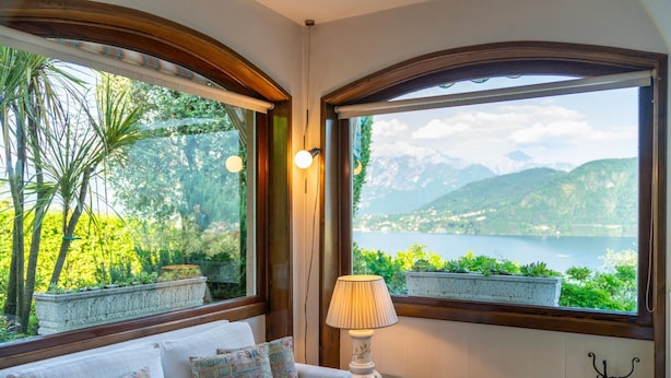 A room with a sofa, a lamp, and large windows offering a view of mountains and a lake. - Ca Furmiga by Wonderful Italy (Tremezzina)