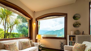 A cozy living room with a large window offering a view of lush greenery and mountains. - Ca Furmiga by Wonderful Italy (Tremezzina)