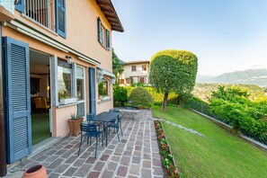 Eine Terrasse mit Steinplatten, Gartenmöbeln und einem gepflegten Garten mit Hecke und Blumen.