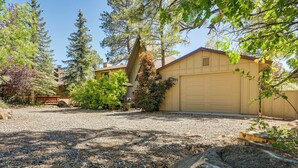 A residential property with a garage, surrounded by trees and a gravel driveway.