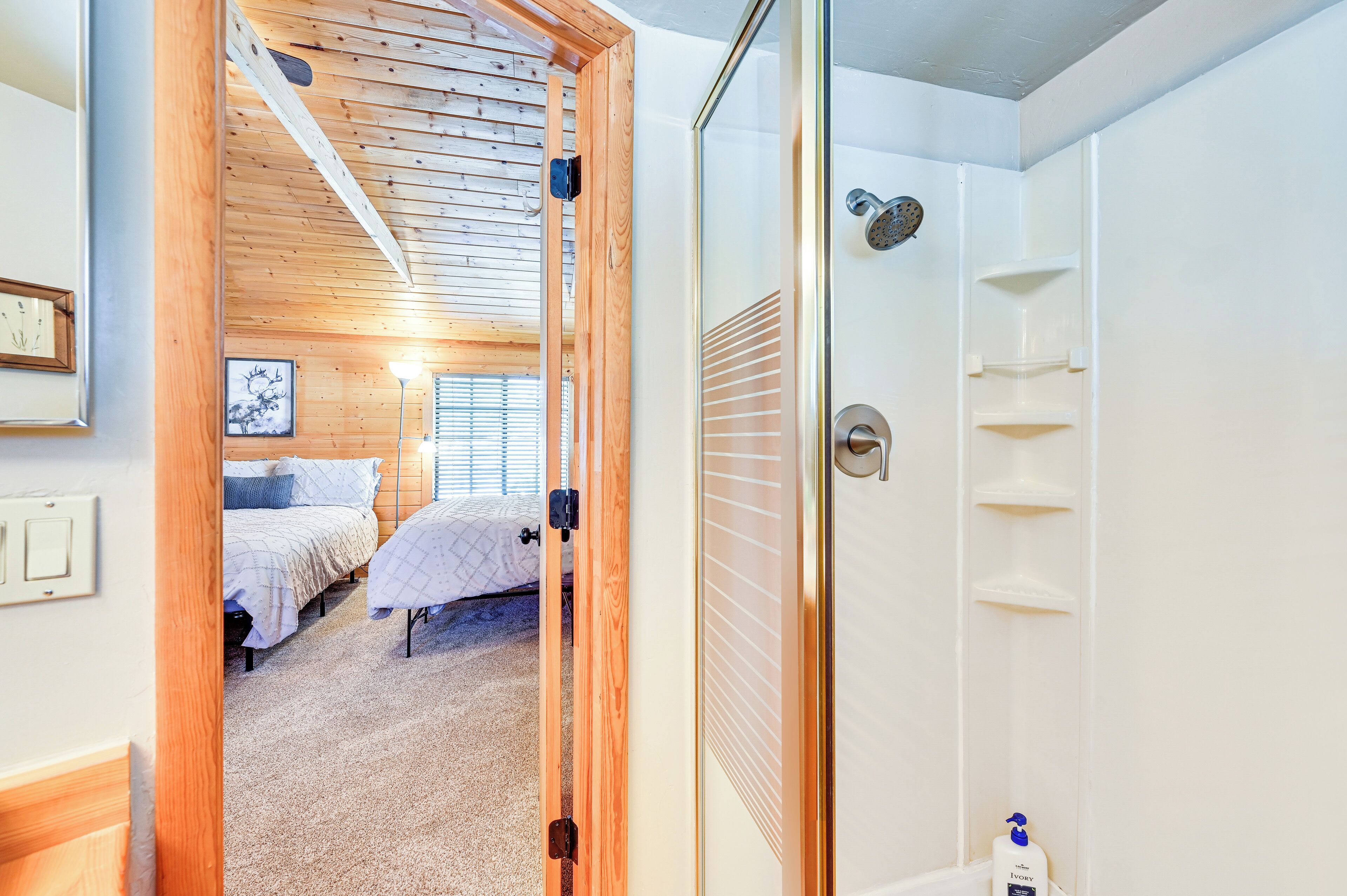 A bedroom with two beds, a wooden ceiling, a glass shower enclosure, and a small shelf with toiletries.