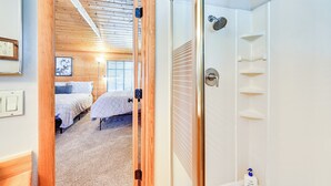 A bedroom with two beds, a wooden ceiling, a glass shower enclosure, and a small shelf with toiletries.