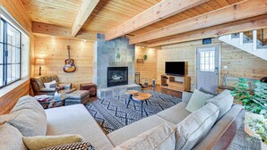 A cozy log cabin interior with a stone fireplace, leather furniture, and a large window.