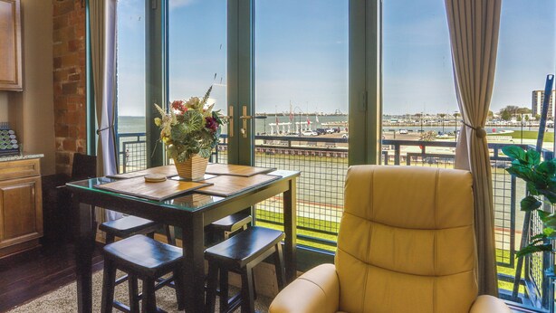 A room with a view of a marina, a dining table with chairs, a yellow armchair, and a potted plant. - Waterfront Sandusky Vacation Rental: Downtown! (Sandusky)