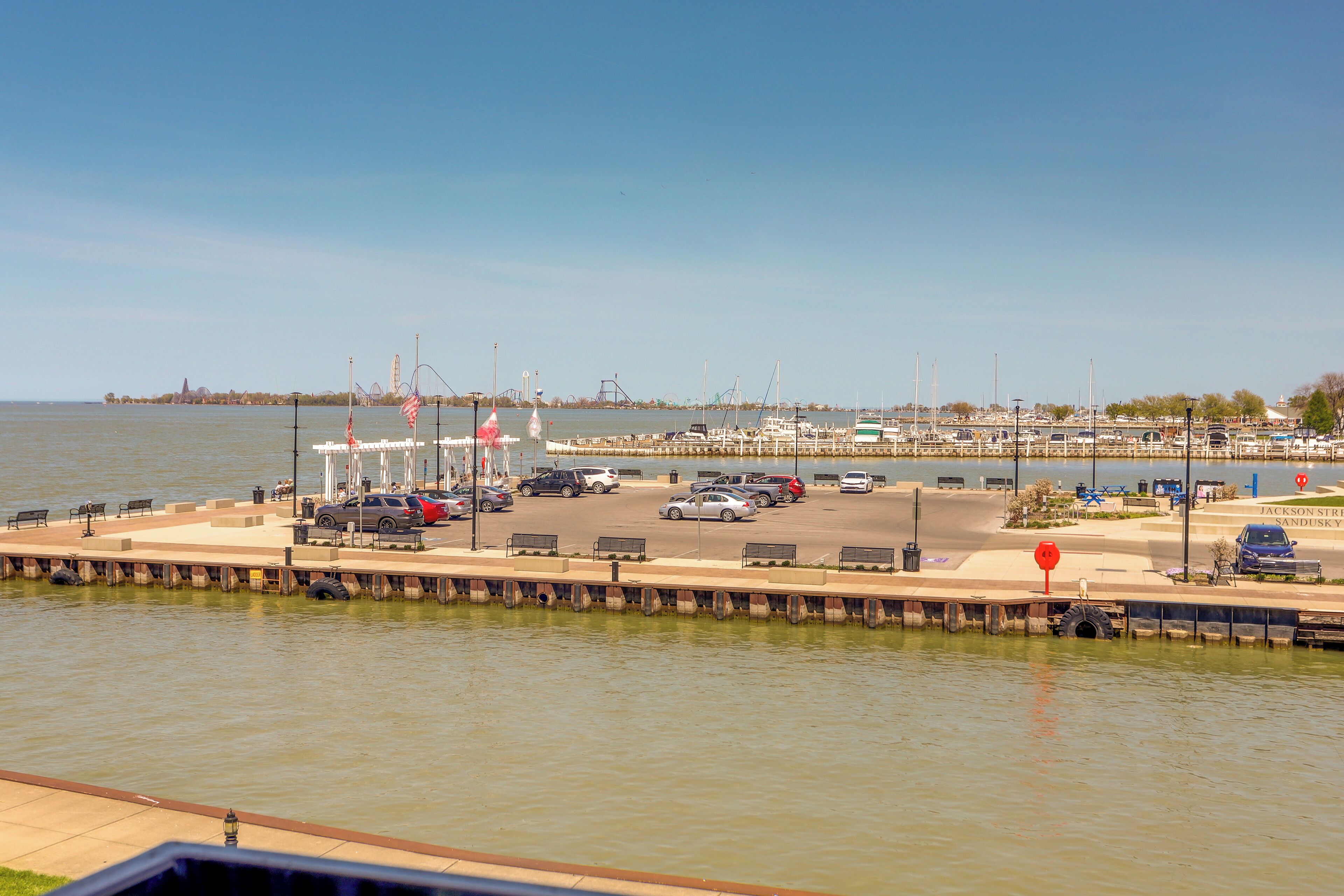A marina with boats docked, a parking area, and a clear view of the water and distant city skyline.