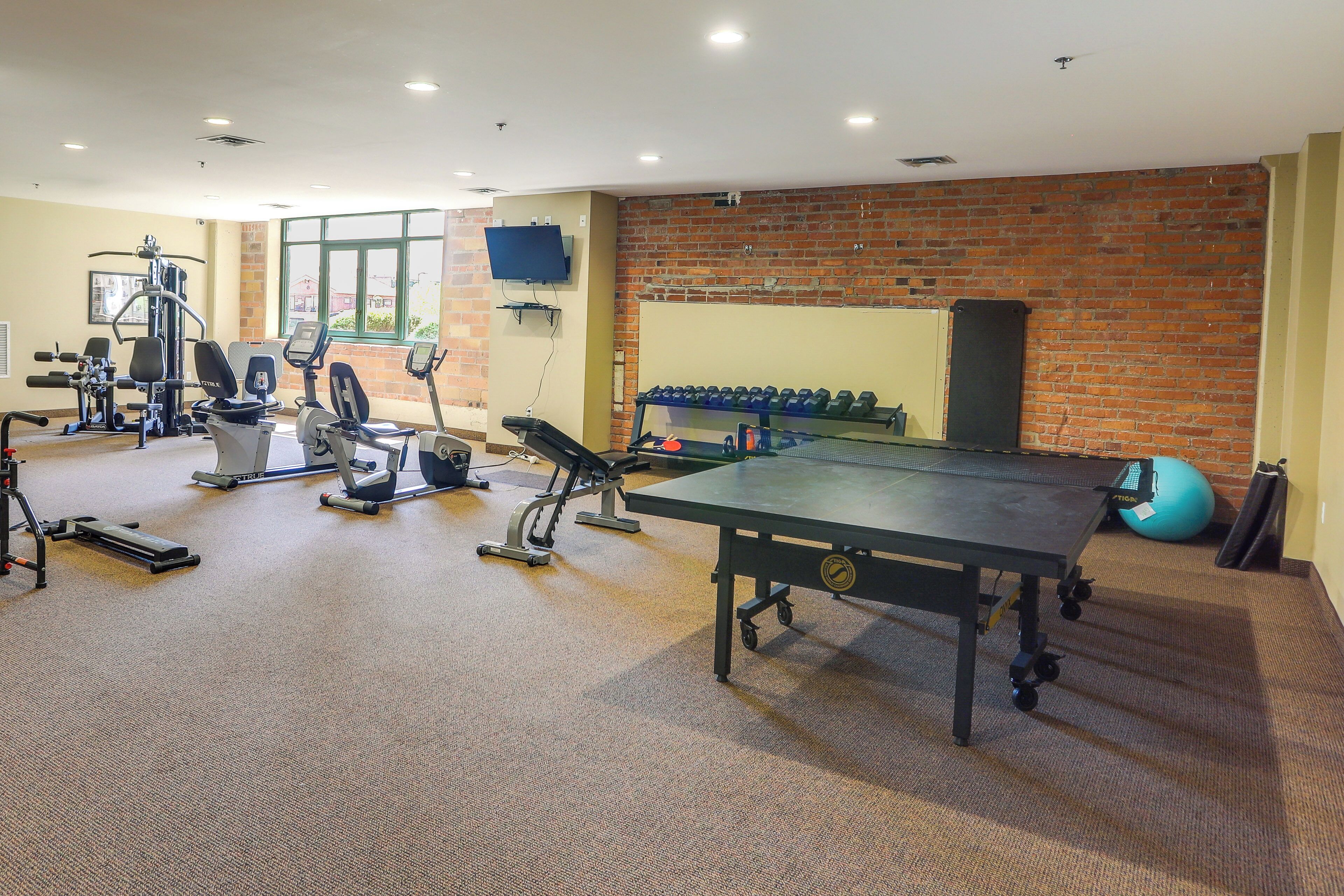 A gym with various exercise equipment, a ping pong table, and a brick wall.
