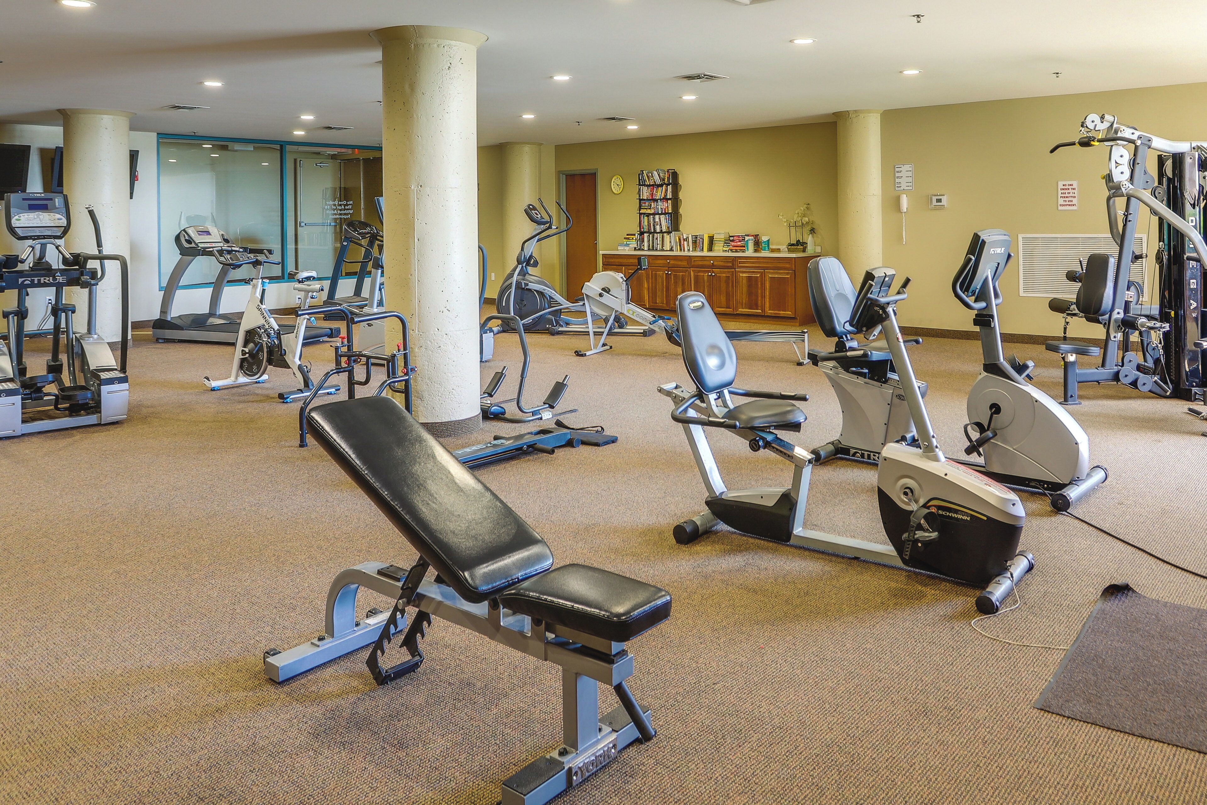 Ein Fitnessstudio mit verschiedenen Trainingsgeräten, darunter Laufbänder, Crosstrainer und Gewichtbänke.