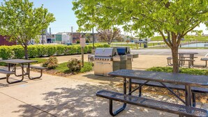 An outdoor patio area with picnic tables, a barbecue grill, and a parking lot in the background. - Waterfront Sandusky Vacation Rental: Downtown! (Sandusky)