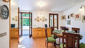 Uma cozinha com armários de madeira, uma mesa de jantar posta para quatro pessoas e vista para o exterior pela porta aberta.