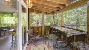 A covered outdoor dining area with a table and chairs, large windows, and a view of the surrounding trees. - Pet-friendly Getaway w/ Porch in Banner Elk! (Banner Elk)