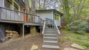 A cabin with a wooden deck, a staircase leading to a second-story balcony, and a stack of firewood. - Pet-friendly Getaway w/ Porch in Banner Elk! (Banner Elk)