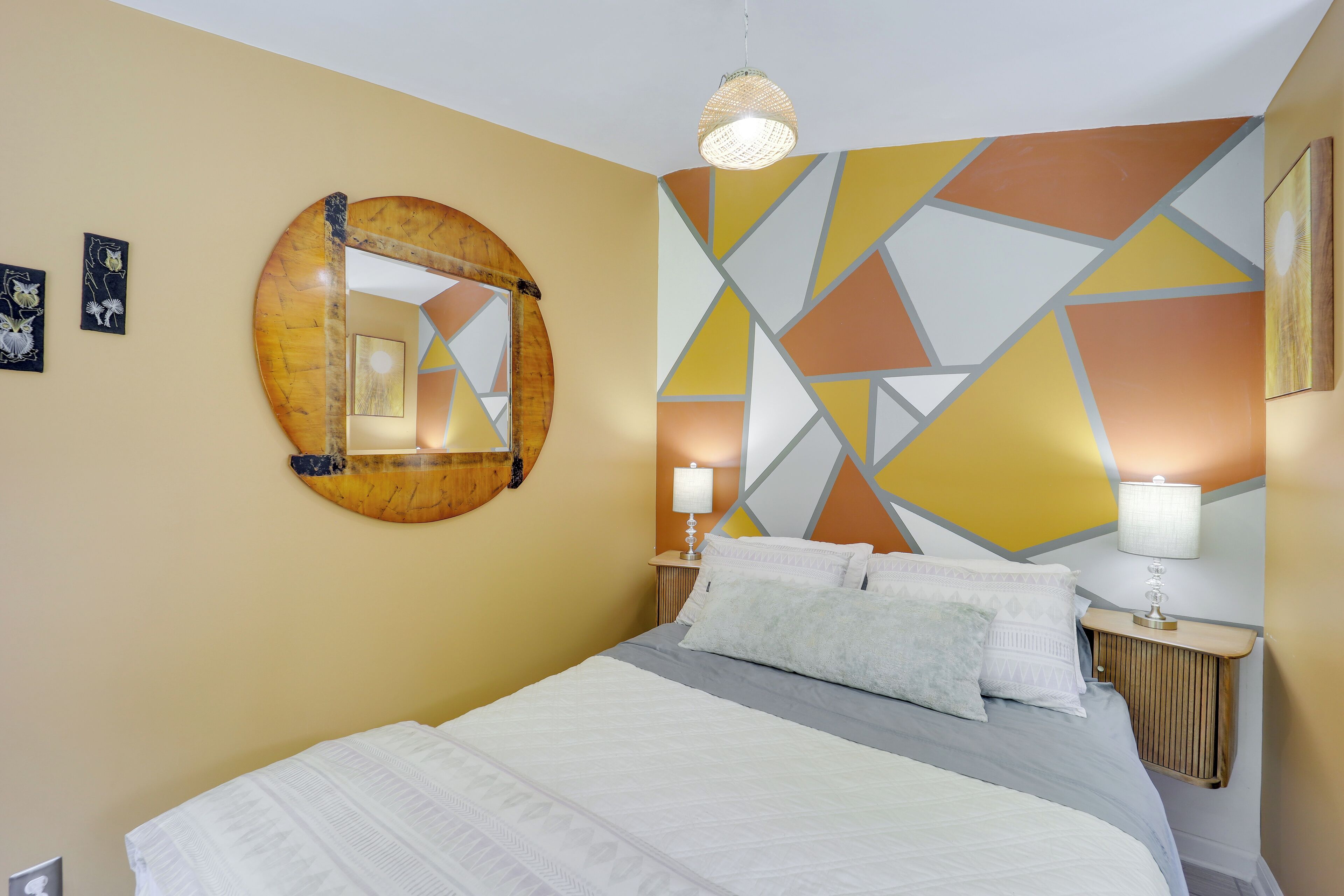 Ein modernes Hotelzimmer mit einem großen Bett, einem runden Spiegel, geometrischer Wandkunst und Nachttischlampen.
