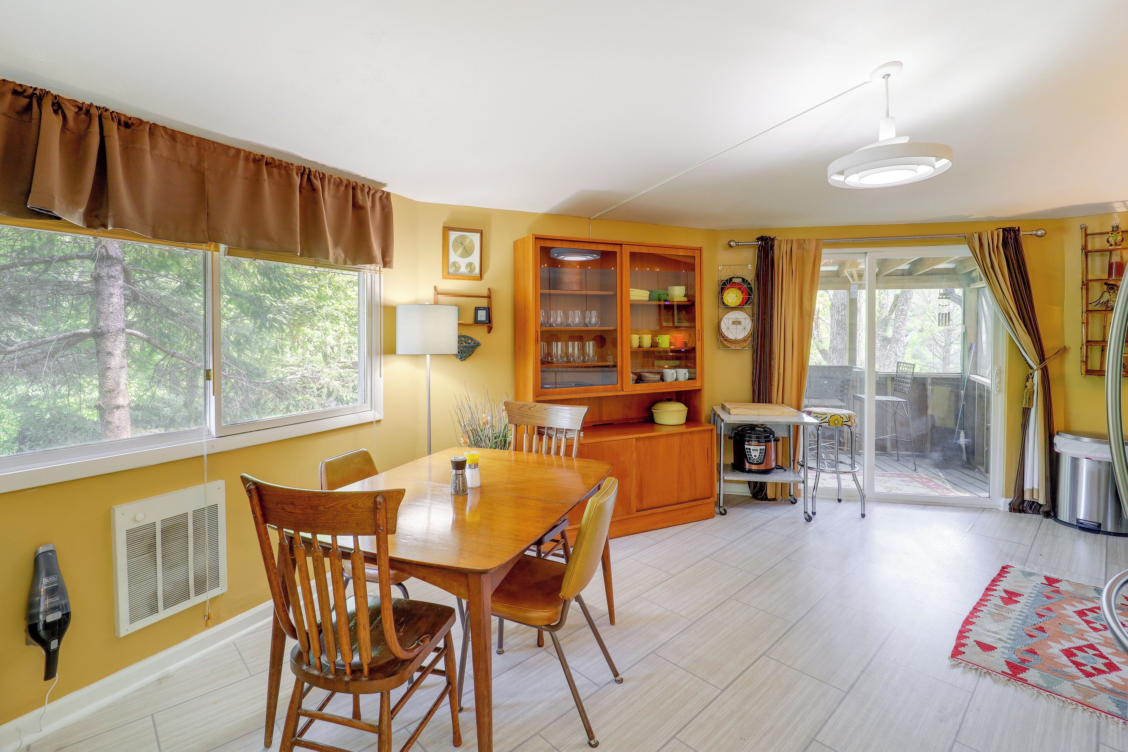 Un comedor con una mesa y sillas de madera, un aparador con puertas de vidrio y vistas al exterior.