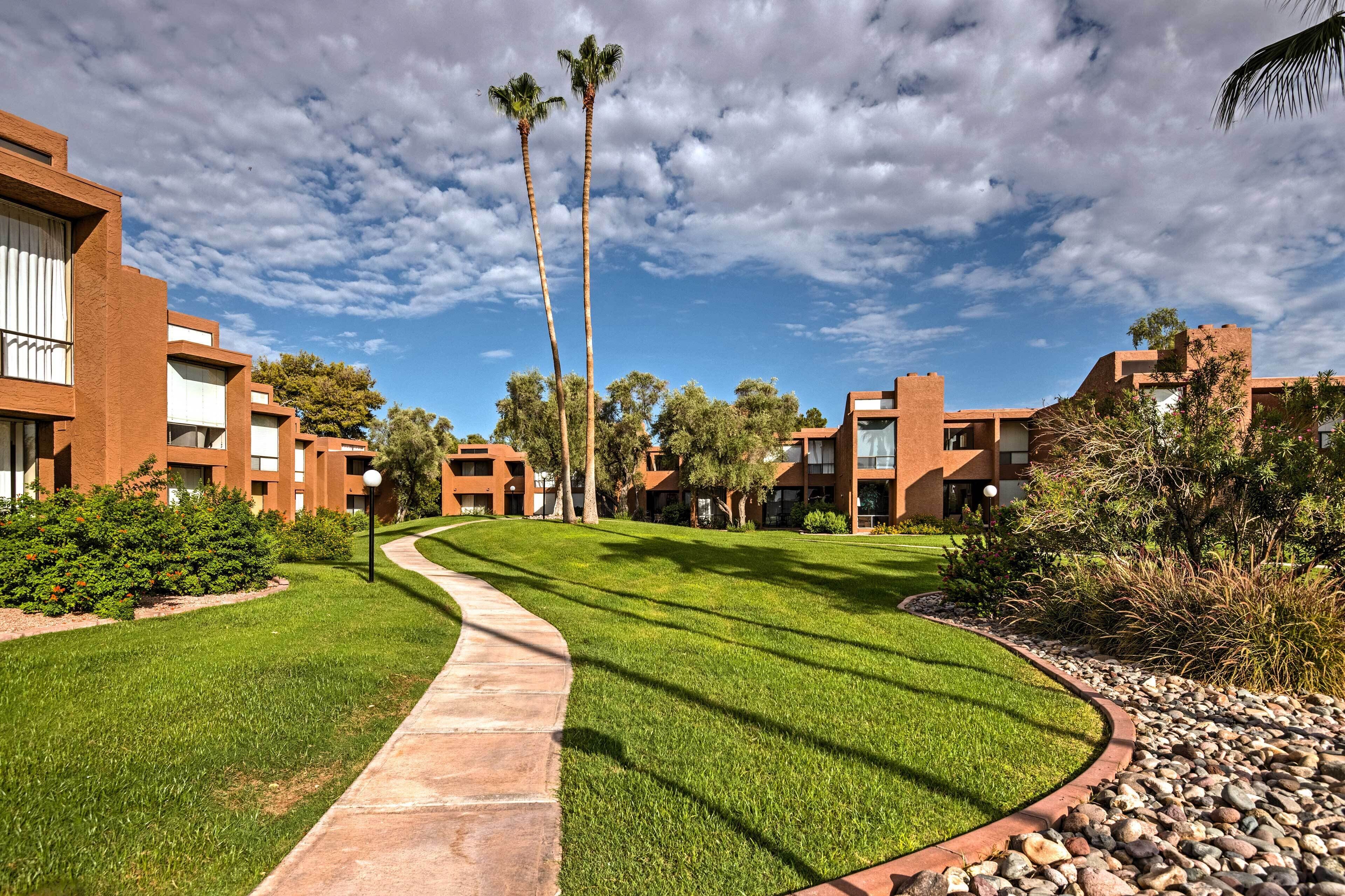 A modern building with a curved pathway, surrounded by well-maintained grass and palm trees.