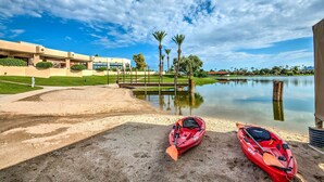 A serene lakeside setting with a red kayak and paddle on the sand, a bridge, and a building with a modern design. - 3 Mi to Old Town: Scottsdale Condo w/ Pool & Lake (Paradise Valley)