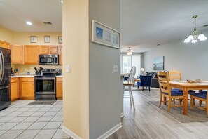 A modern kitchen with wooden cabinets, stainless steel appliances, and a dining area with a wooden table and blue chairs. - Myrtle Beach Golf Retreat w/ Pool Access! (Myrtle Beach)