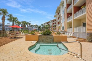A pool area with lounge chairs and umbrellas, surrounded by palm trees and a multi-story building with balconies. - Waterside Village Cottage 3220 (Port St. Joe)