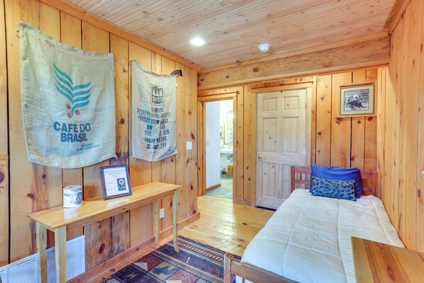 Una habitación de madera con una cama, un banco y una puerta. Hay dos tapices en la pared.