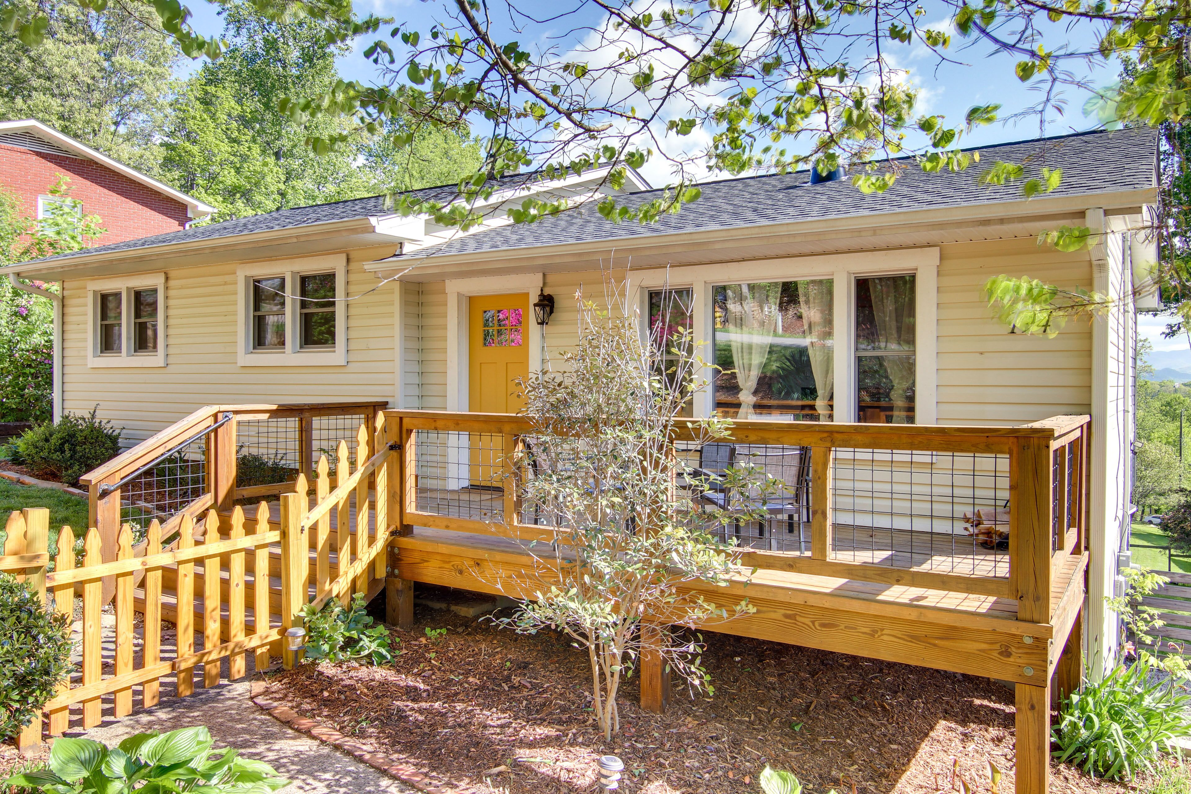 A single-story house with a wooden deck, a small tree, and a yellow door.