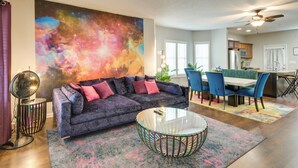 A modern living room with a dark blue sofa, a glass coffee table, and a colorful abstract painting on the wall. - Pet-friendly Davenport Home - Near Casino & Golf (Davenport)