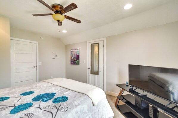 A bedroom with a bed, a ceiling fan, a TV, and a door.