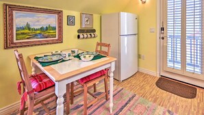 A dining area with a table set for four, chairs, a refrigerator, and a door with blinds. - Riverside Tree House Suite w/ Balcony & Grill (Payson)