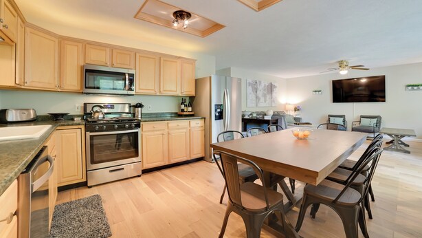 A modern kitchen with wooden cabinets, stainless steel appliances, a dining area with a wooden table and chairs, and a ceiling fan. - Rapid City Cottage w/ Deck: 1/4 Mi to Torch Lake! (Rapid City)