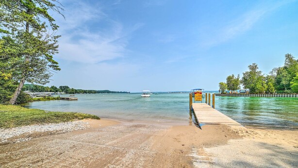 Une plage avec une jetée en bois qui s’avance dans des eaux calmes, entourée de verdure et sous un ciel dégagé.