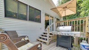 Une terrasse avec des chaises en osier, un barbecue et une bouteille de propane.