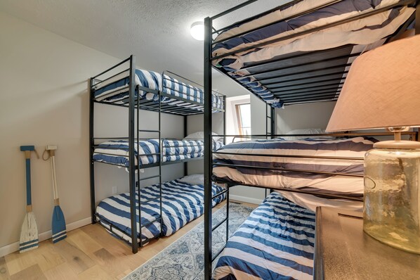 A dormitory room with bunk beds, a wooden floor, a patterned rug, and a large metal container.